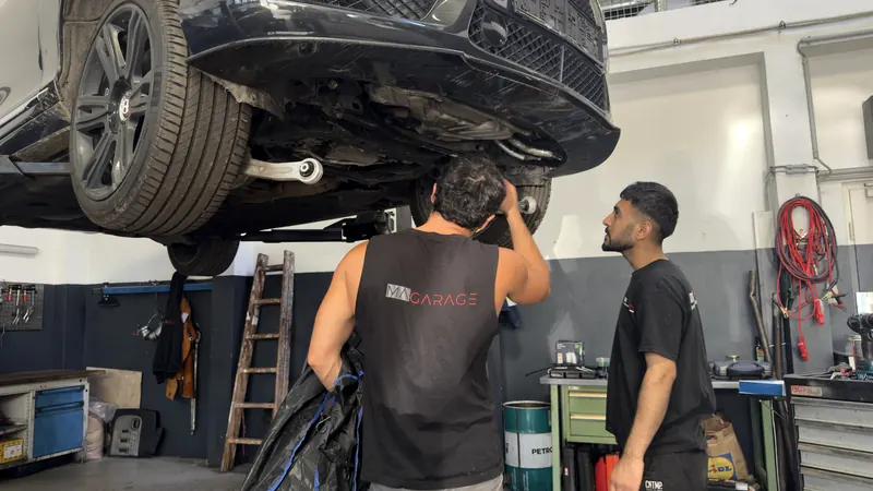 Fahrzeug auf der Hebebühne, zwei Mechaniker der Magarage kontrollieren den Unterboden