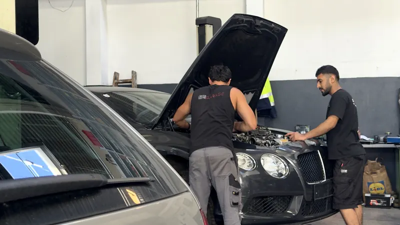 Zwei Mitarbeiter der Magarage prüfen gemeinsam den Motorraum eines Fahrzeugs