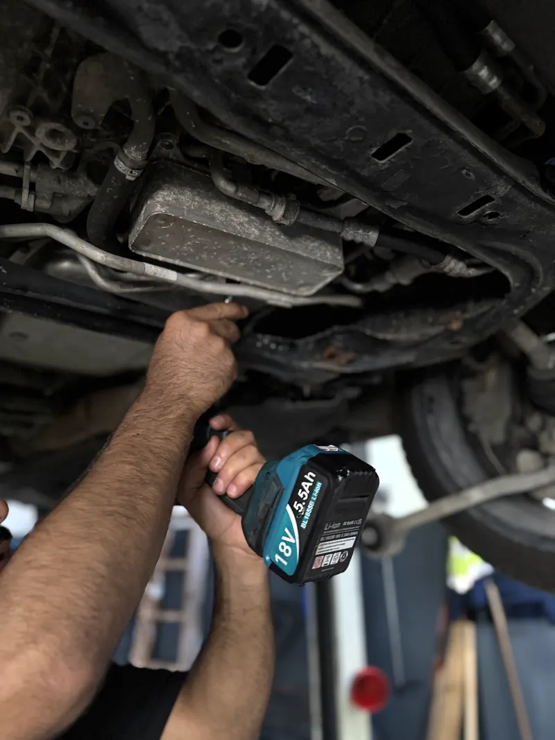 Mechaniker löst Schrauben am Unterboden eines angehobenen Fahrzeugs in der Magarage