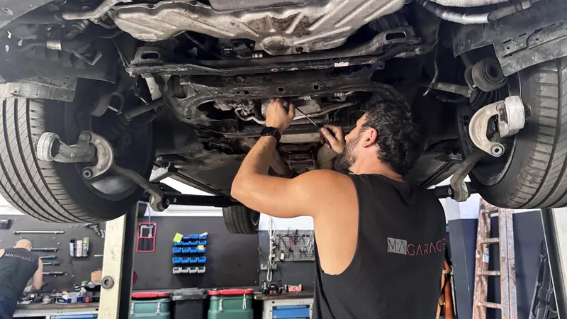 Mechaniker schraubt am Unterboden eines Fahrzeugs auf der Hebebühne in Wien Liesing