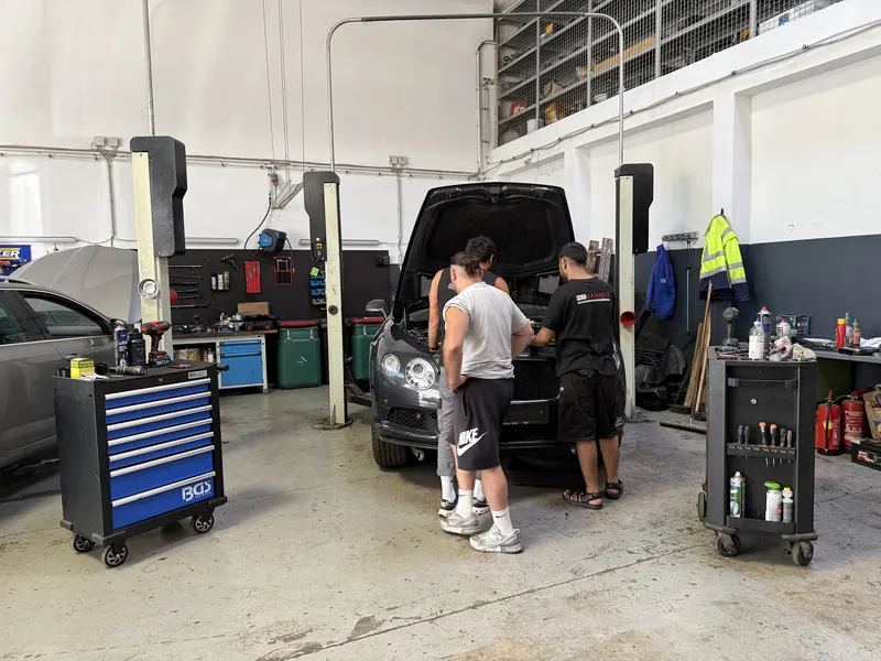 Mitarbeiter der Magarage arbeiten gemeinsam an einem Fahrzeug in der Halle
