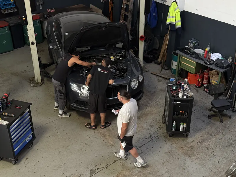 Drei Mechaniker der Magarage bei der Arbeit an einem Fahrzeug in der Werkstatthalle