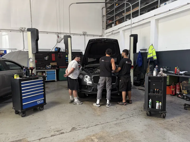 Drei Mechaniker arbeiten gleichzeitig an einem Fahrzeug in der Halle der Magarage